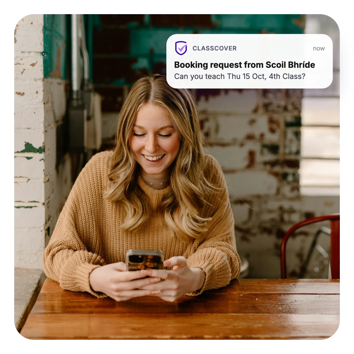 A substitute teacher smiling at a ClassCover booking request from Scoil Bhríde on her phone